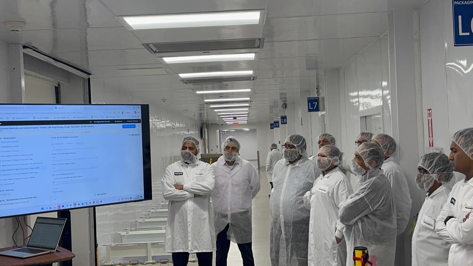 Group of pharma operators in cleanroom gowns watching the Leucine MES batch record demo in a packaging corridor