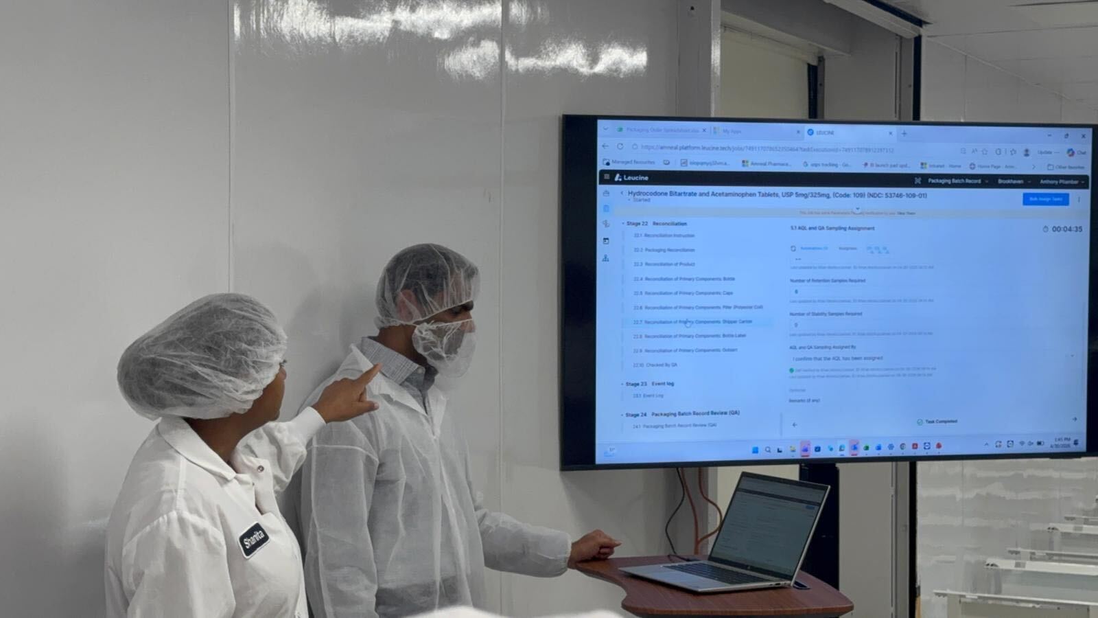 Two operators in cleanroom gowns at a wall-mounted screen reviewing a Leucine MES Packaging Batch Record stage